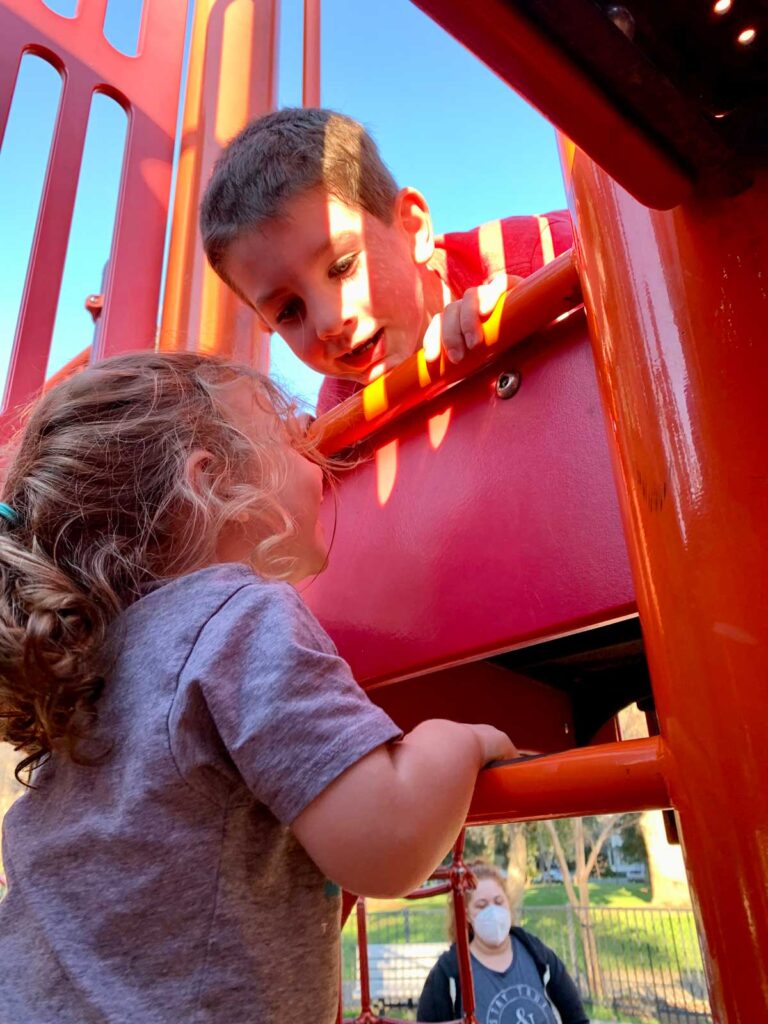 two kids helping each other climb on a play structure