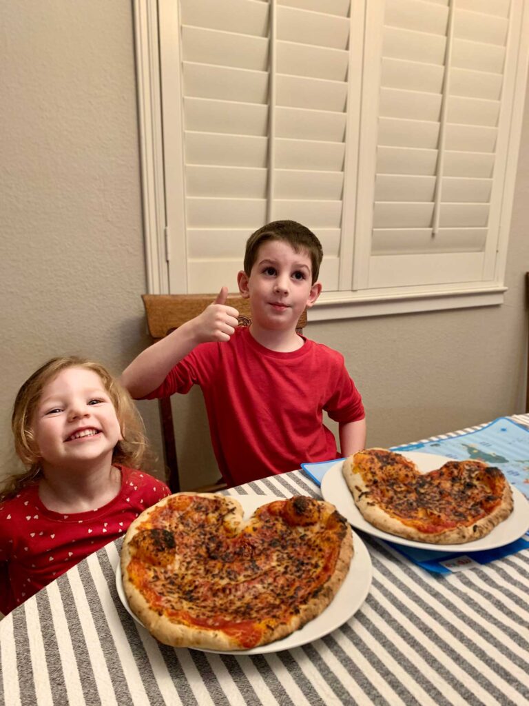 two kids with heart-shaped pizzas on the table in front of them