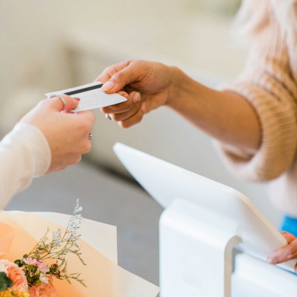 female hand giving a credit card to another female hand at a checkout terminal