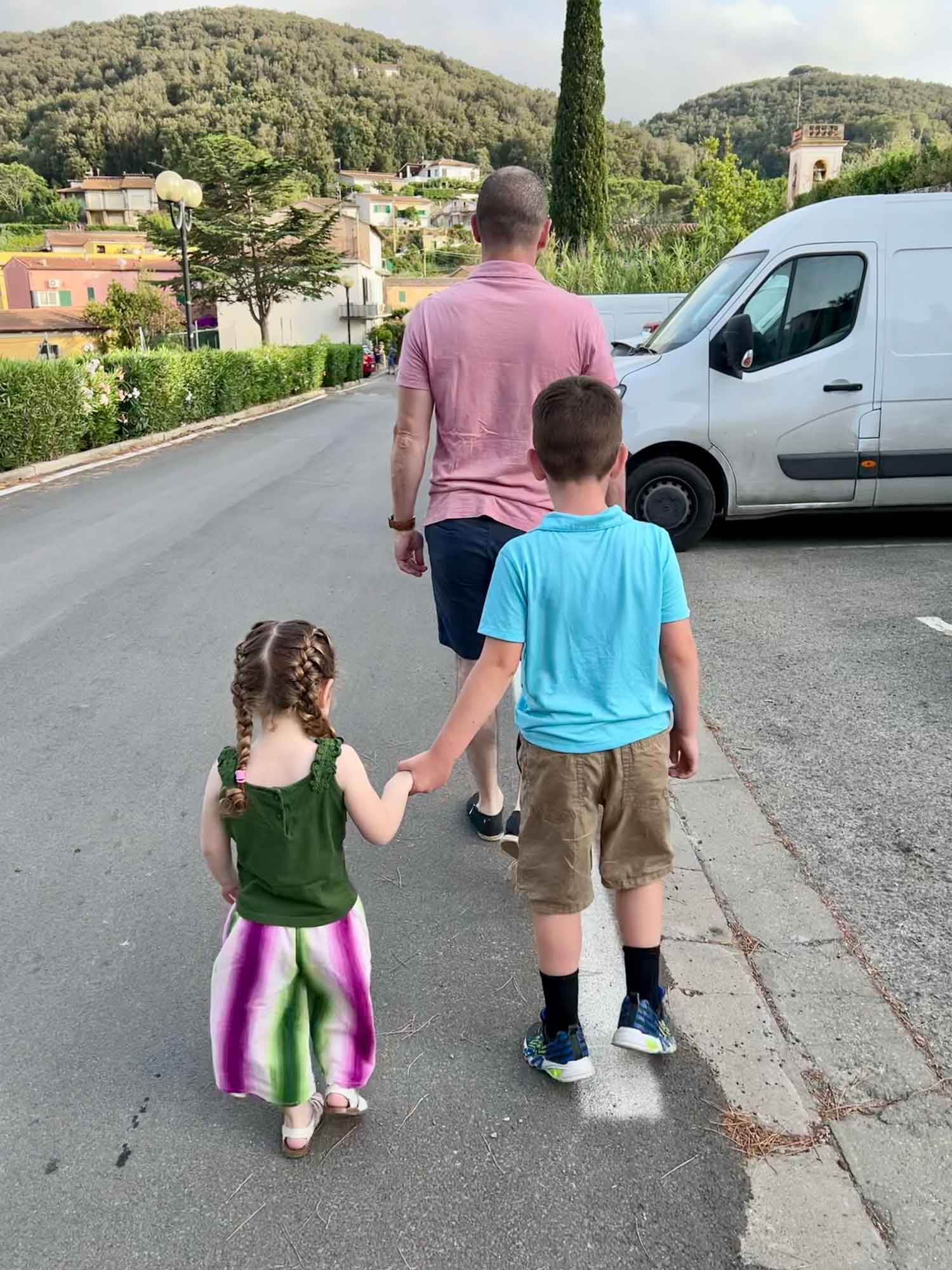 Dad leading two kids holding hands down a road