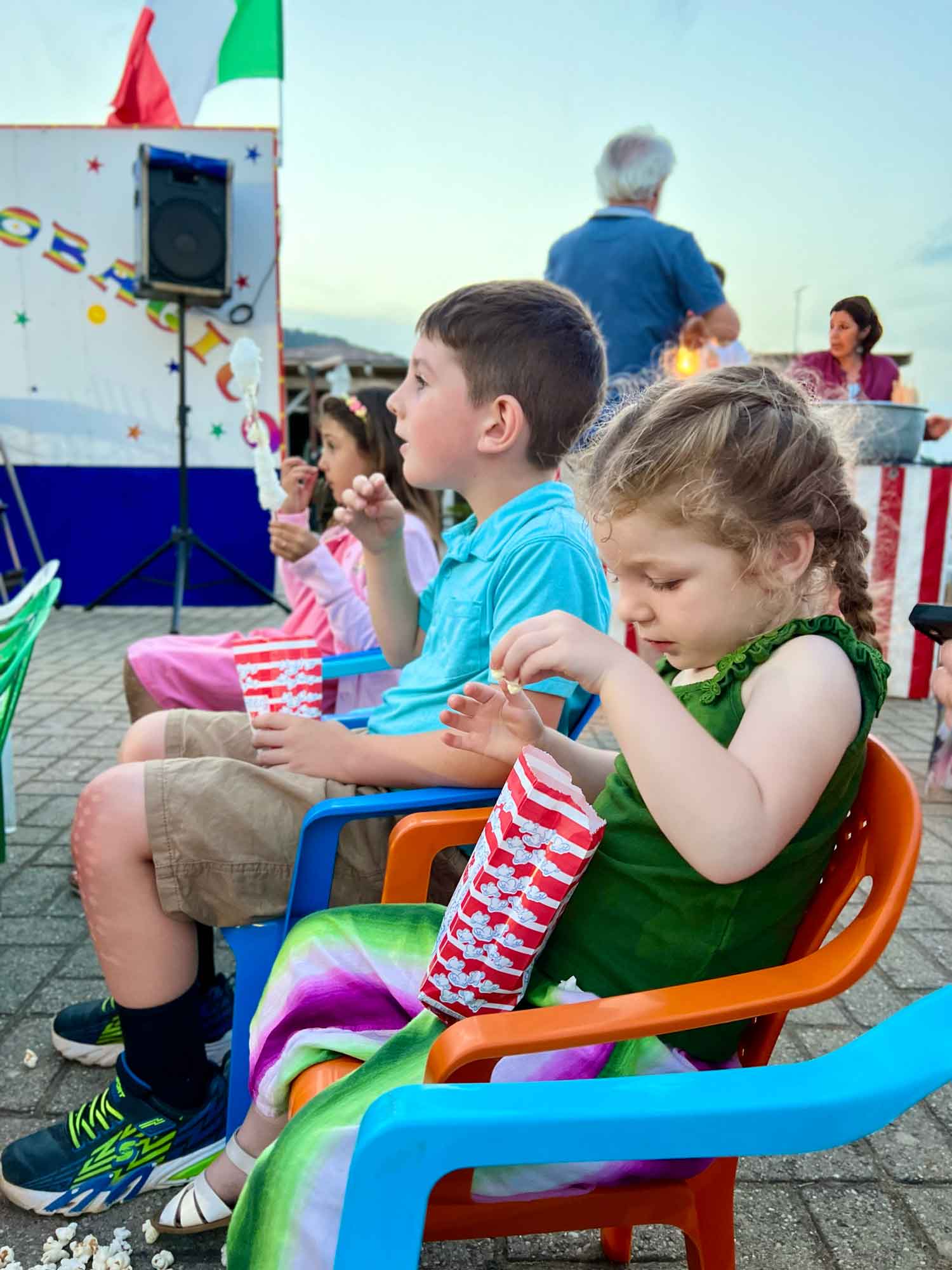 two kids sitting in chairs eating popcorn from a carnival
