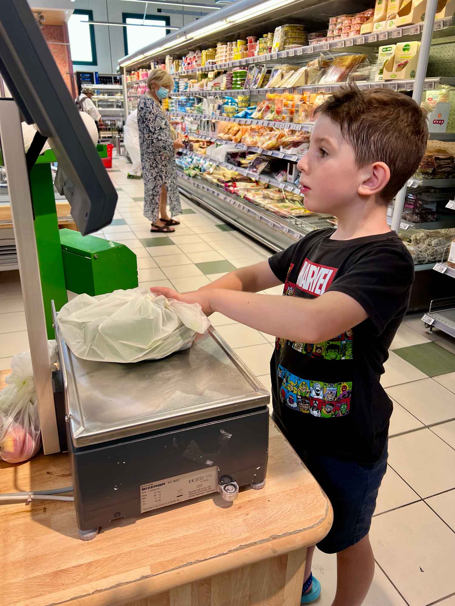 boy standing at a produce scale in a grocery store