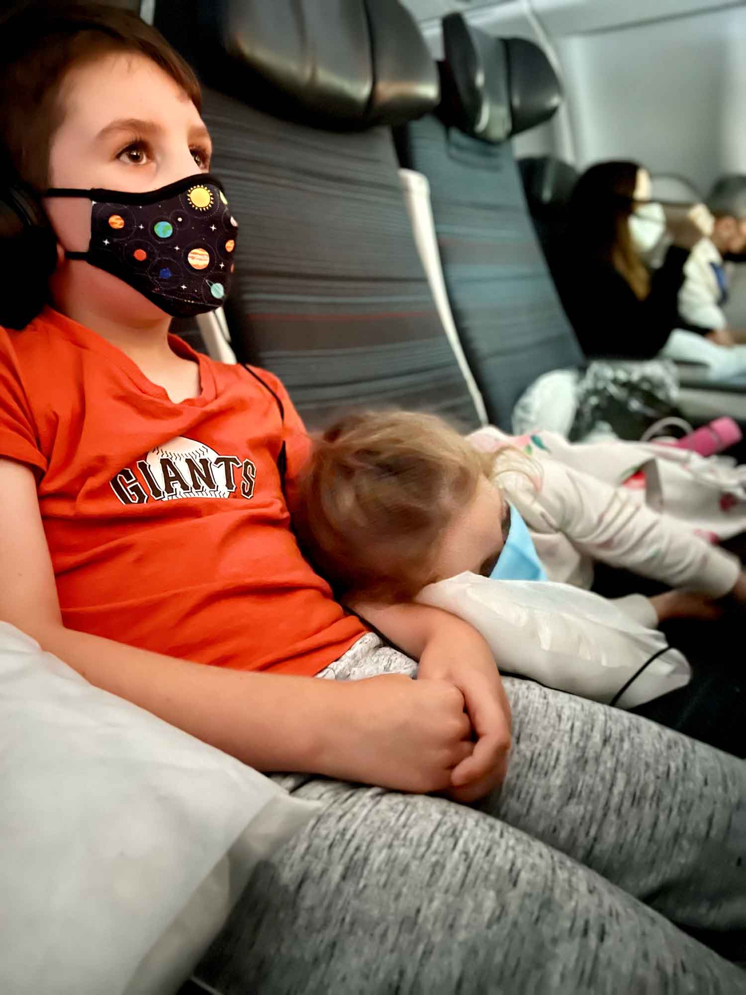 little sister lays on big brother in an airplane