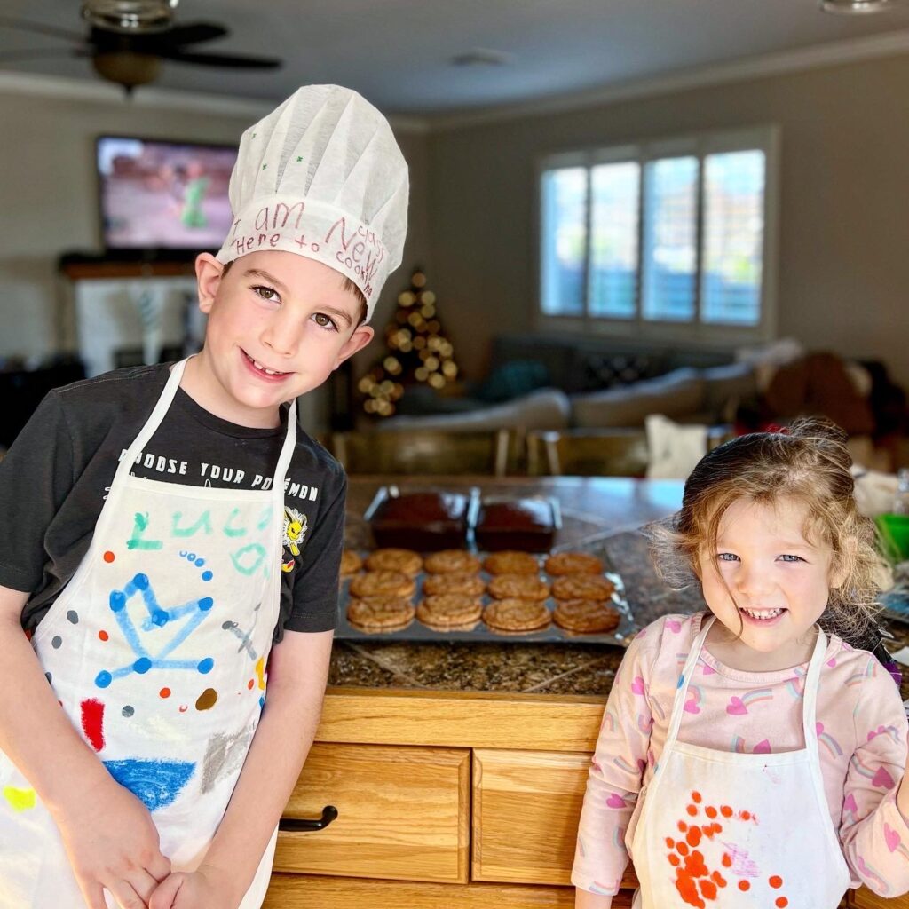 two kids in aprons beside a sheet of homemade cookies