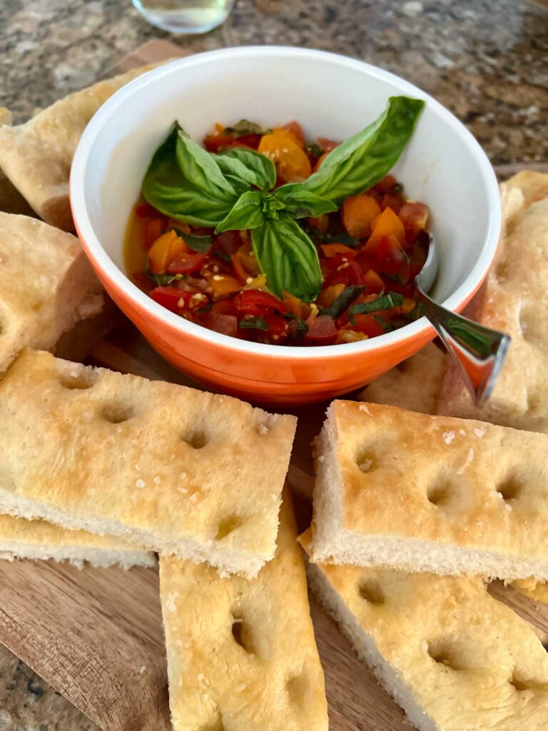 bruschetta with a sprig of basil in a bowl surrounded by focaccia rectangles