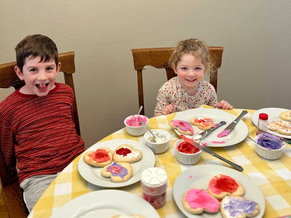 two kids sitting at a table decorating Valentine's cookies